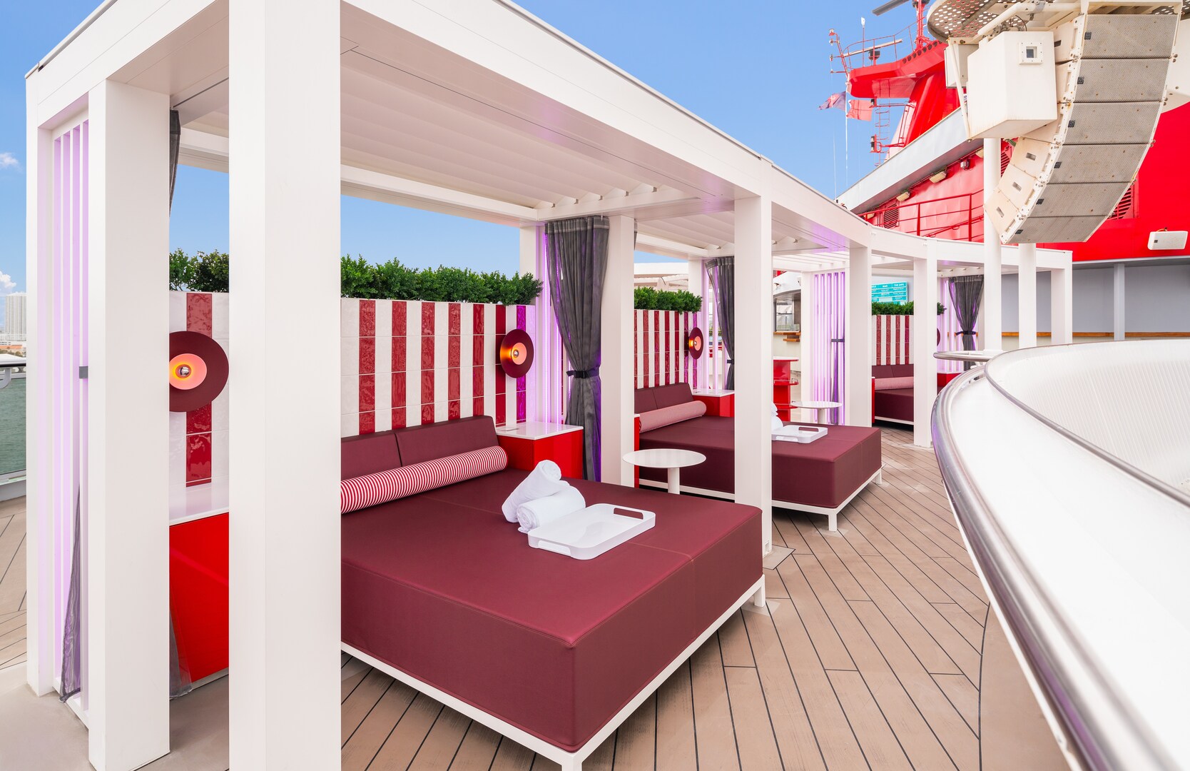 Cabanas with maroon daybeds and white towels on the Scarlet Lady cruise ship.