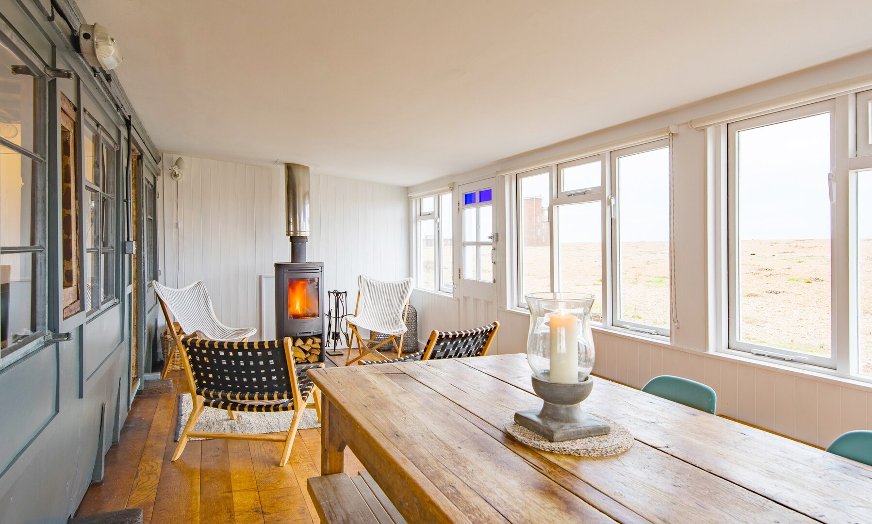 Beachfront cottage interior with wood-burning stove and large windows overlooking the beach.