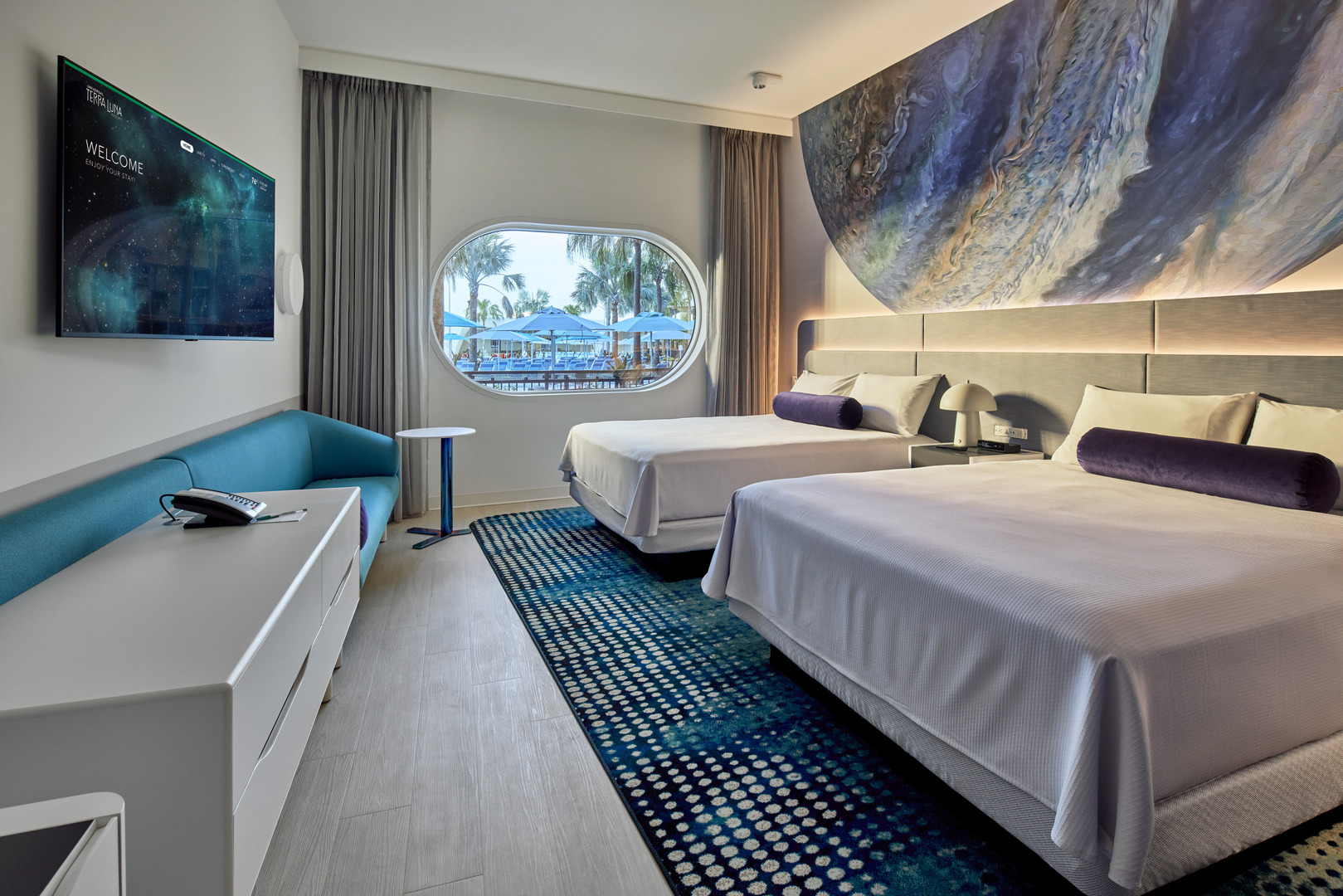 Universal Terra Luna Resort guest room with two beds, a teal sofa, and a large window overlooking a pool.