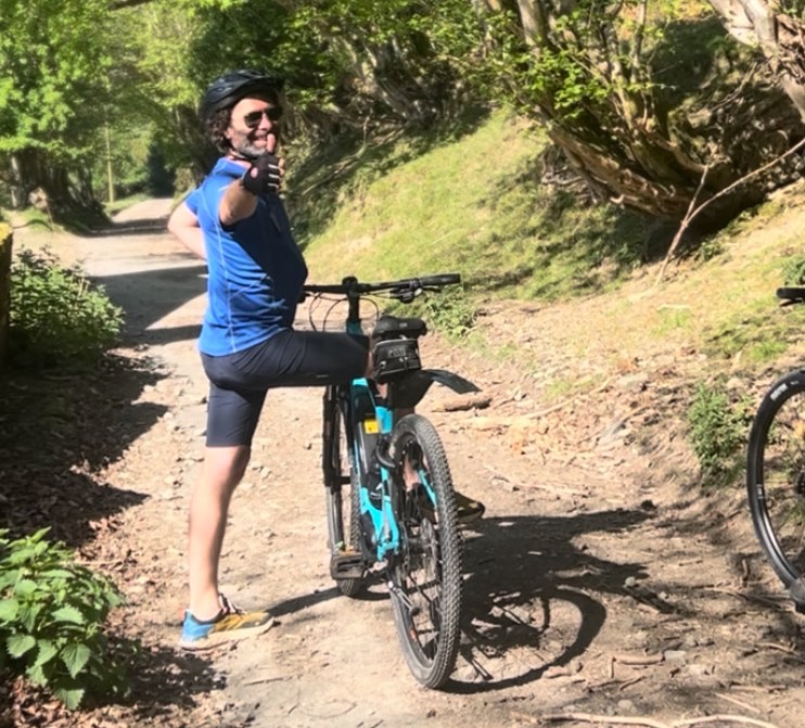 Man giving thumbs up while standing next to his bicycle on a trail.
