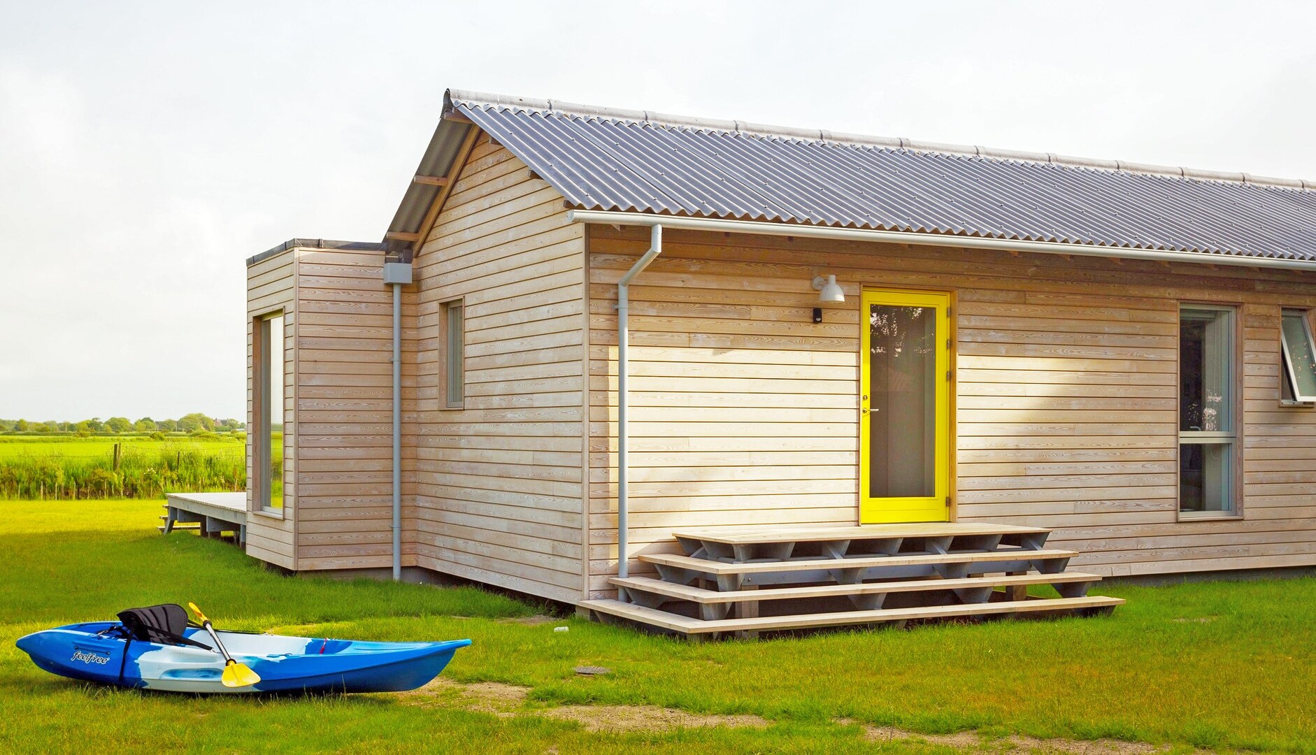 Wooden cottage with yellow door and kayak in front.