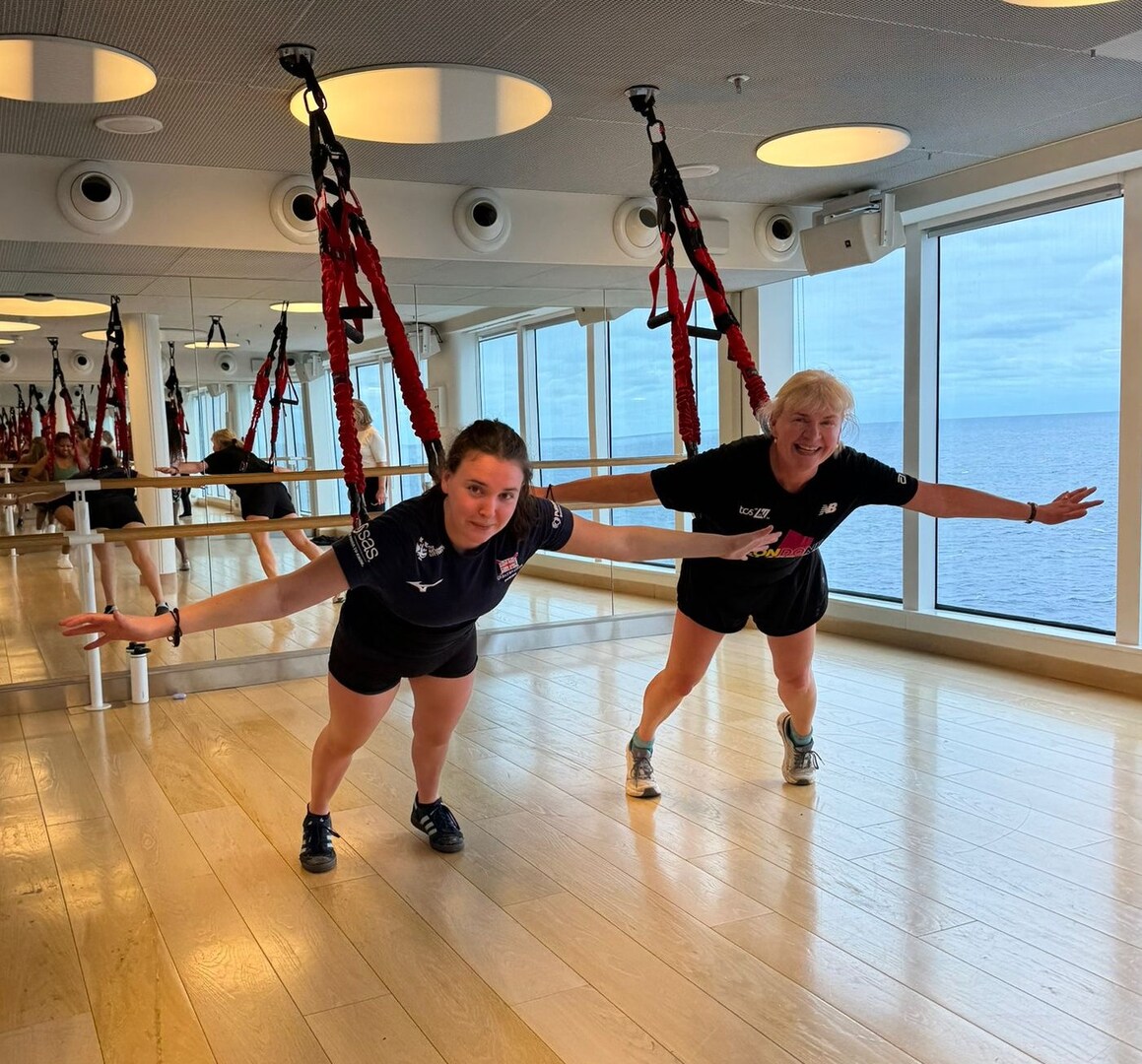 Two women using suspension training equipment in a gym.